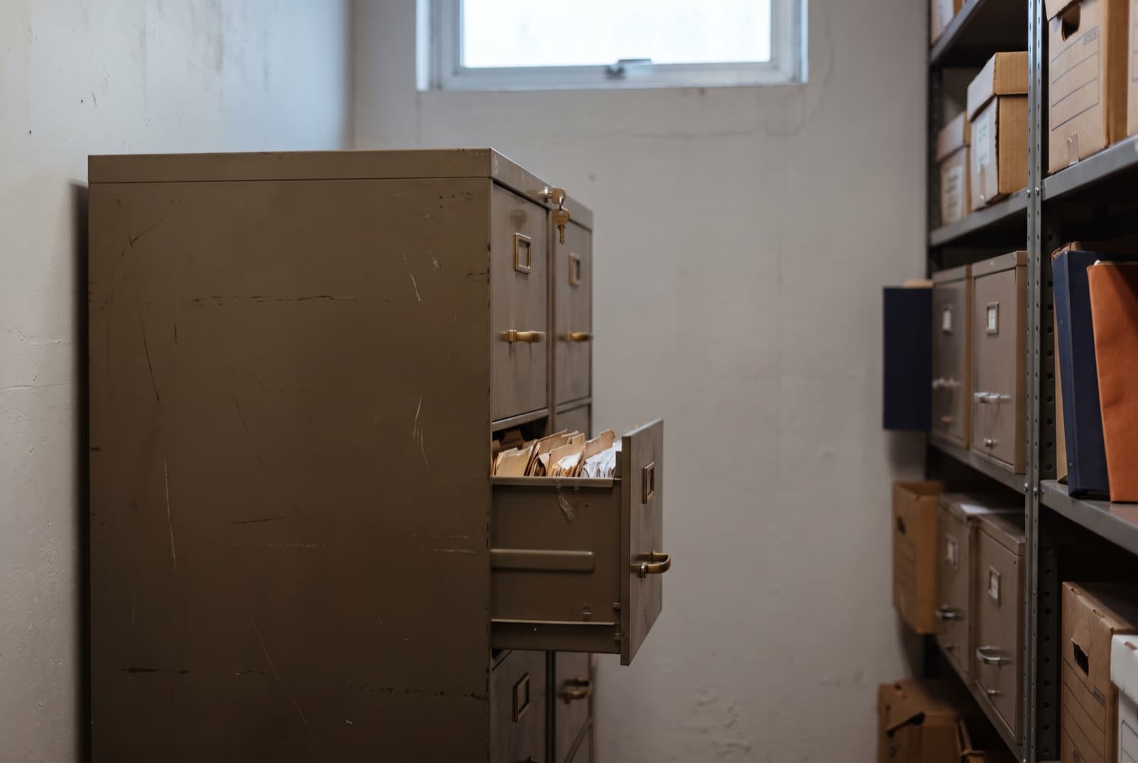 A steel archive cabinet with a key in its lock, one drawer slightly ajar showing the tops of manila folders.