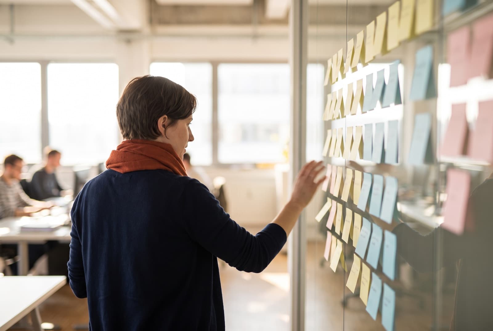 A coordinator moving one paper note among columns of notes on a glass wall.