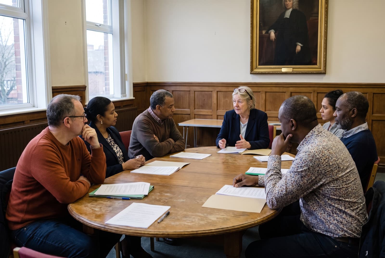 Trustees around an oval table in a wood-panelled committee room, papers in front of each of them.