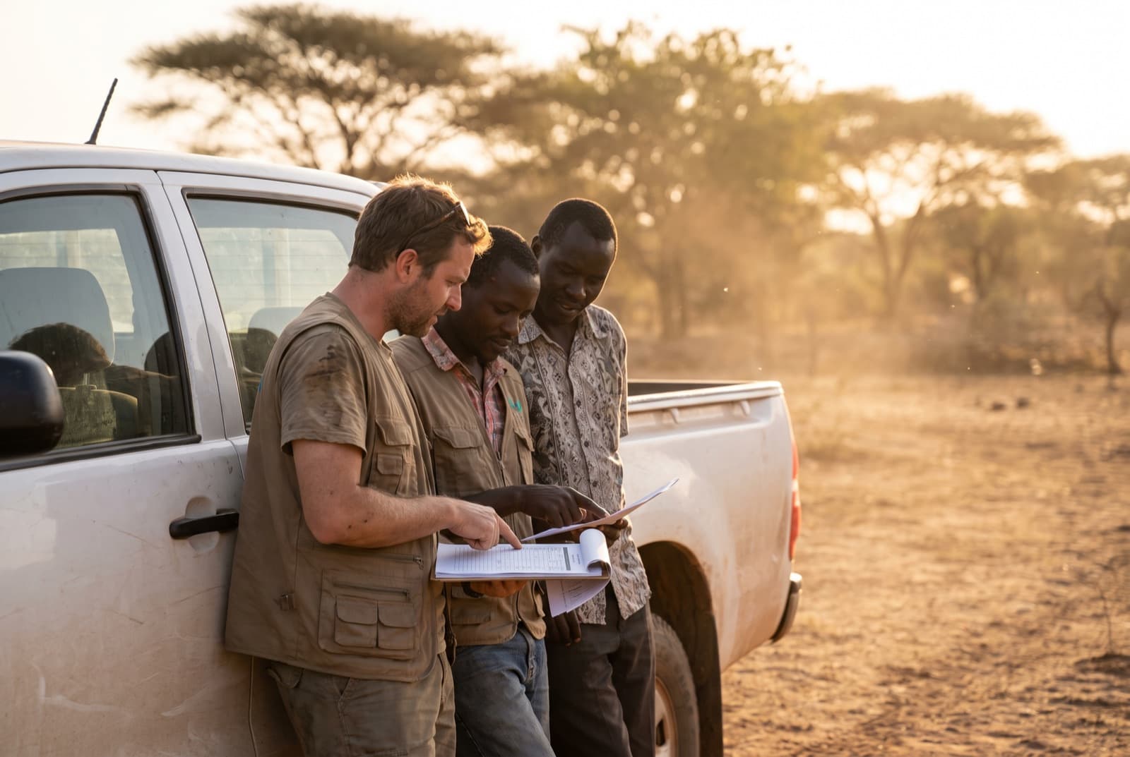 Two programme staff and a local partner reading a clipboard of forms together at a rural site.